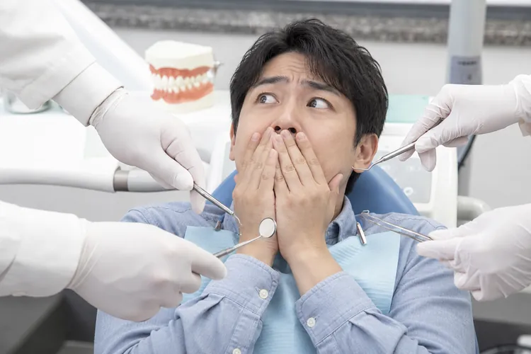 診療器具を持つ手に囲まれ、驚いて口を覆う男性